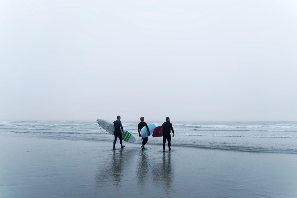 Image of three people with surf boards walking into the ocean in Vancouver Island