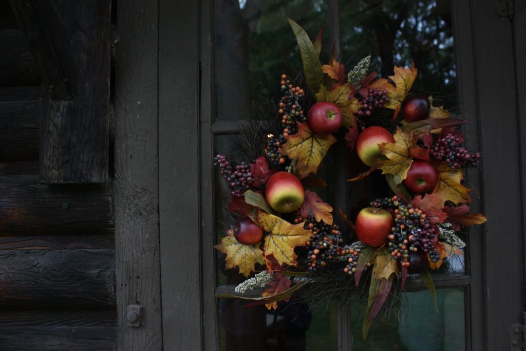 Image of an autumn wreath with leaves, apples, and fall berries hanging on the front door of a Ucluelet house